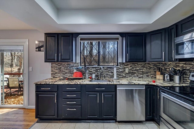 kitchen with tasteful backsplash, light stone counters, appliances with stainless steel finishes, a raised ceiling, and a sink