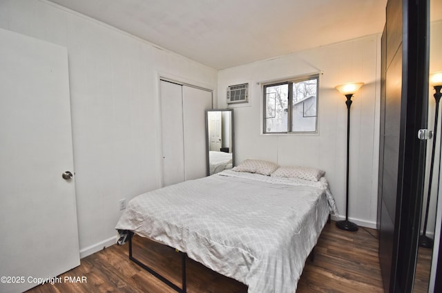 bedroom featuring dark wood-style floors, baseboards, a closet, and an AC wall unit