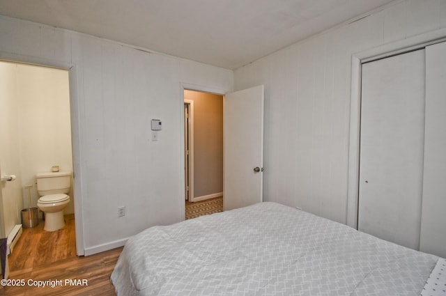 bedroom featuring connected bathroom, wood finished floors, baseboards, a closet, and baseboard heating