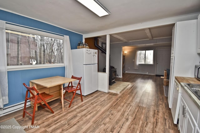 kitchen featuring breakfast area, a wood stove, wood finished floors, white appliances, and beamed ceiling