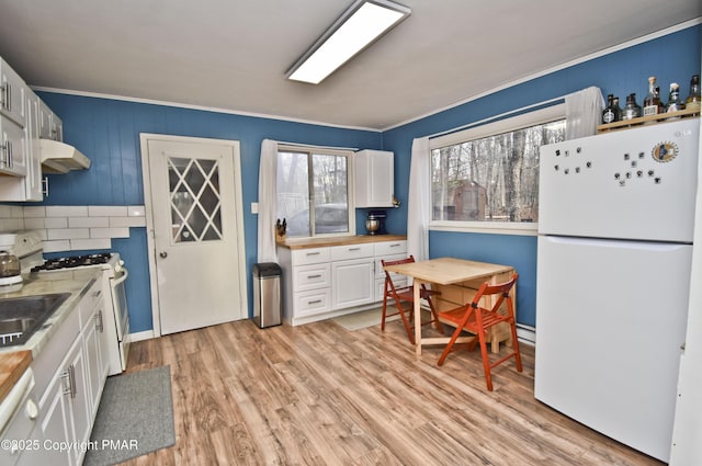 kitchen with under cabinet range hood, white appliances, white cabinetry, light countertops, and light wood finished floors