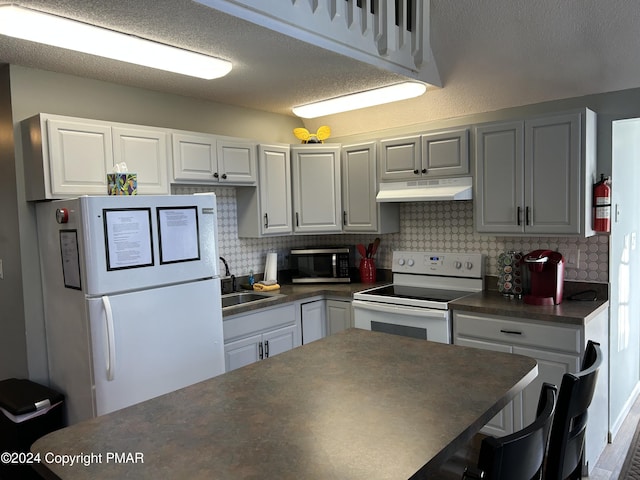 kitchen featuring dark countertops, backsplash, a sink, white appliances, and under cabinet range hood