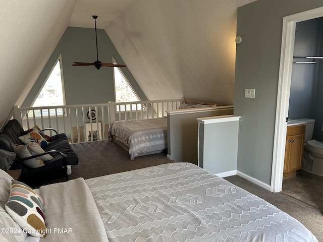 bedroom with dark colored carpet, lofted ceiling, baseboards, and ensuite bathroom