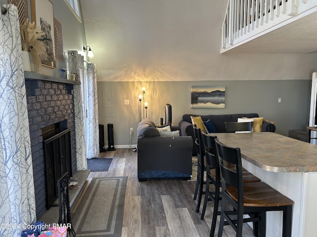 living room featuring a textured ceiling, a stone fireplace, wood finished floors, and baseboards