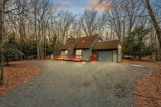 rustic home with driveway, a shingled roof, a chimney, an attached garage, and a deck