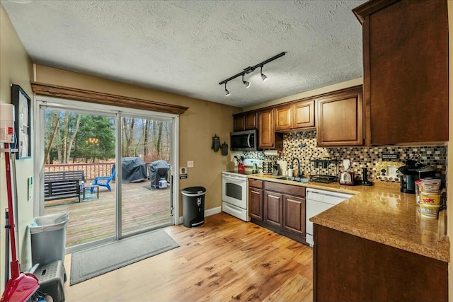 kitchen with white appliances, a sink, a textured ceiling, light wood-style floors, and backsplash