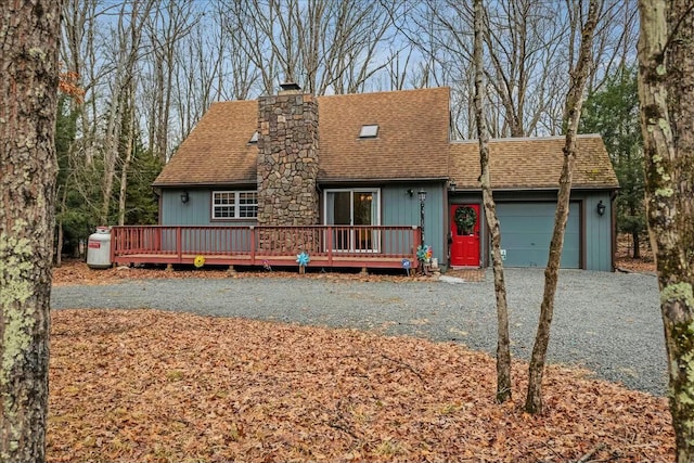 view of front of property featuring a garage, a shingled roof, driveway, a wooden deck, and a chimney