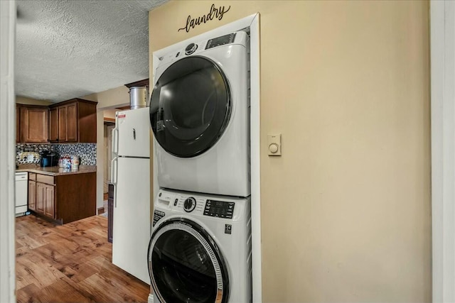 clothes washing area featuring a textured ceiling, light wood-style flooring, and stacked washer and clothes dryer