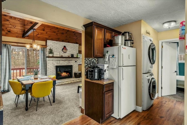 kitchen featuring dark wood-style flooring, stacked washer / drying machine, freestanding refrigerator, a fireplace, and a chandelier