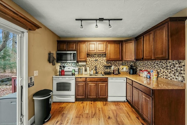 kitchen featuring light wood-type flooring, white appliances, a sink, and backsplash