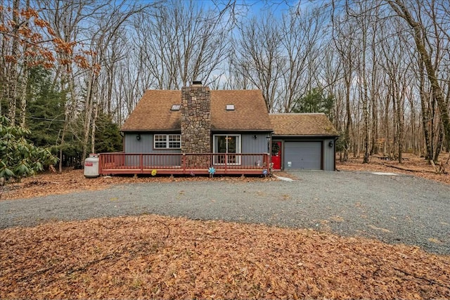 view of front of home featuring gravel driveway, roof with shingles, a chimney, an attached garage, and a deck