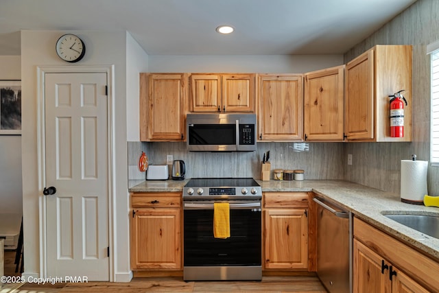 kitchen with light stone countertops, tasteful backsplash, appliances with stainless steel finishes, and light wood-style floors