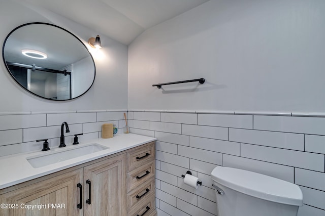 bathroom with wainscoting, vanity, toilet, and tile walls