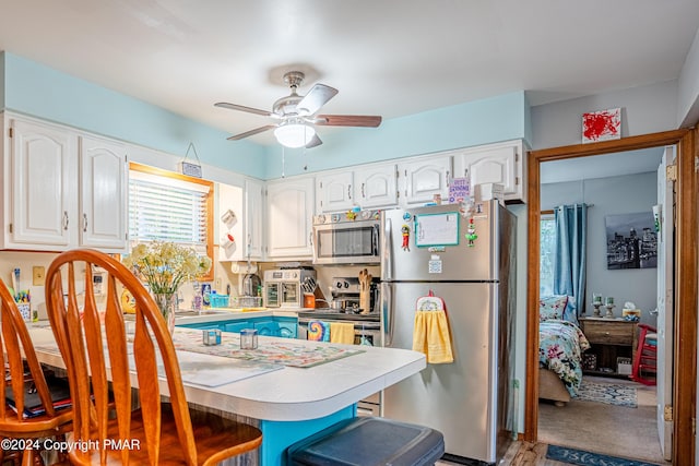 kitchen with appliances with stainless steel finishes, white cabinets, a kitchen breakfast bar, and a ceiling fan