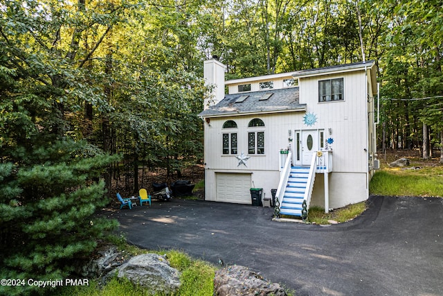 view of front facade featuring a shingled roof, driveway, a chimney, and an attached garage