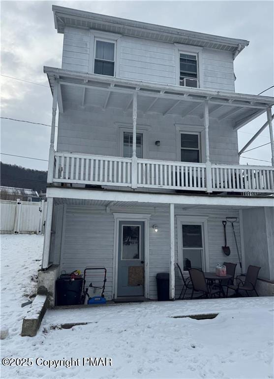 snow covered back of property with a balcony and covered porch