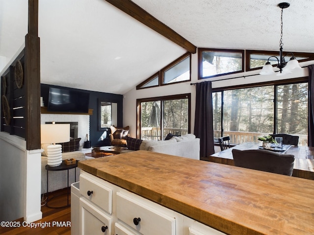 kitchen with butcher block countertops, white cabinetry, vaulted ceiling with beams, hanging light fixtures, and an inviting chandelier