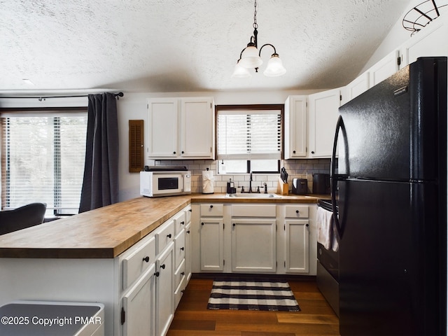 kitchen featuring decorative light fixtures, sink, white cabinets, dark hardwood / wood-style flooring, and black fridge