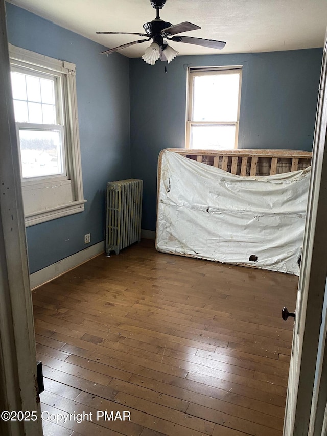 unfurnished bedroom featuring ceiling fan, radiator, and hardwood / wood-style floors