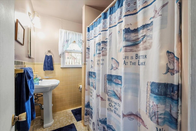 bathroom with curtained shower, tile patterned flooring, a wainscoted wall, a sink, and tile walls