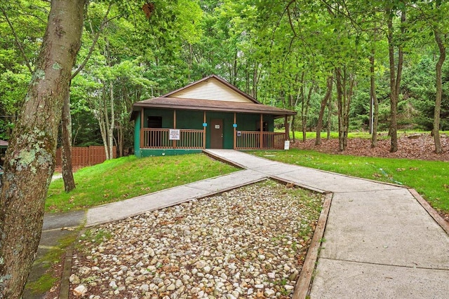 chalet / cabin featuring a wooded view, a front yard, covered porch, and fence