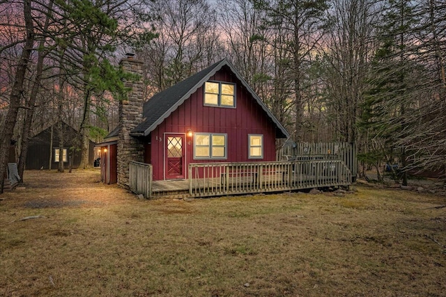 back of property at dusk with board and batten siding, a lawn, a chimney, and a deck