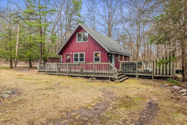 rear view of property with board and batten siding, an outdoor structure, a chimney, and a deck