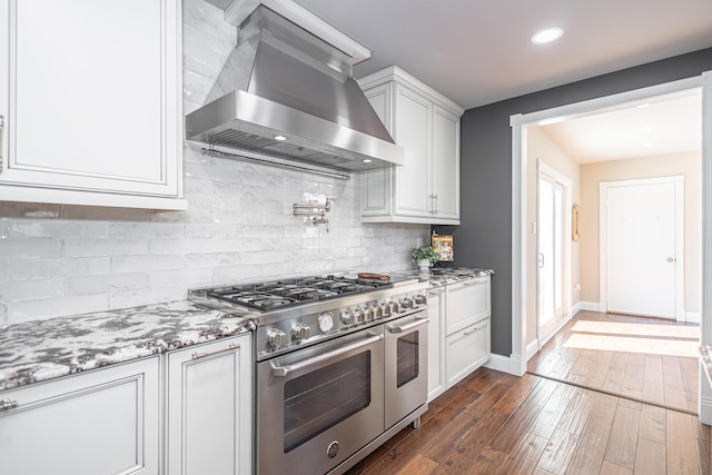 kitchen featuring dark wood-type flooring, backsplash, white cabinetry, wall chimney range hood, and range with two ovens