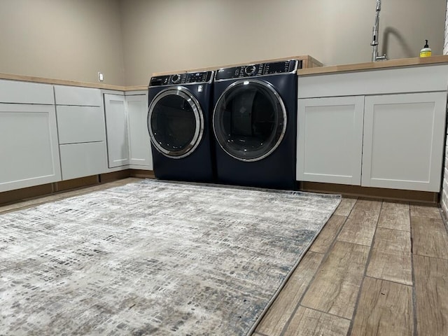 clothes washing area featuring cabinet space, light wood-type flooring, and washer and clothes dryer