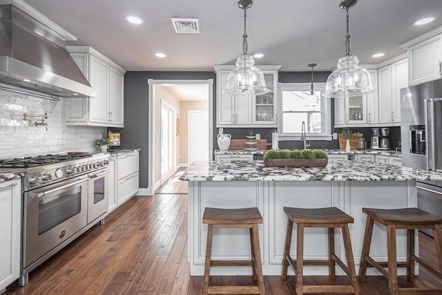 kitchen with glass insert cabinets, high quality appliances, dark wood finished floors, and wall chimney range hood