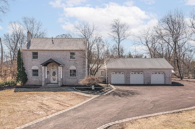 colonial house featuring an attached garage, brick siding, a chimney, and driveway