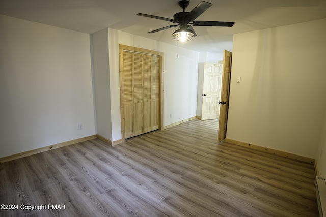 unfurnished bedroom featuring a baseboard heating unit, wood finished floors, a ceiling fan, baseboards, and a closet