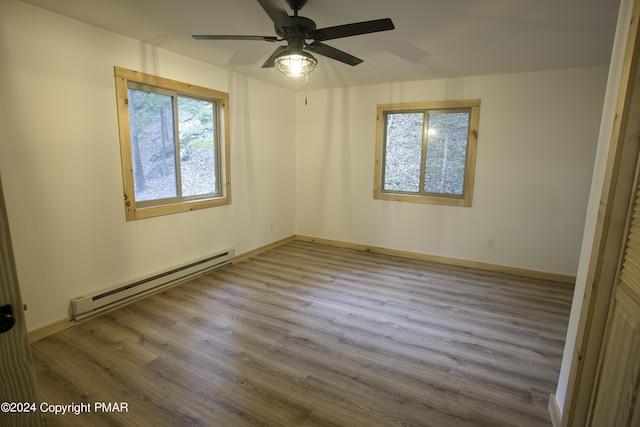 spare room featuring a ceiling fan, baseboards, a baseboard heating unit, and wood finished floors