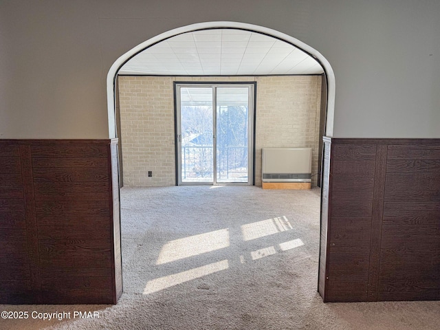 empty room with brick wall, carpet, and a wainscoted wall