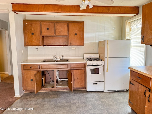 kitchen with brown cabinetry, a sink, wood walls, white appliances, and tile patterned floors