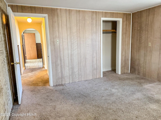 unfurnished bedroom with arched walkways, carpet flooring, and wooden walls