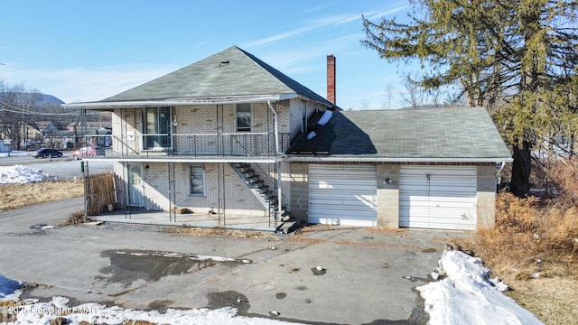 view of front of property with an attached garage, brick siding, stairs, driveway, and a chimney