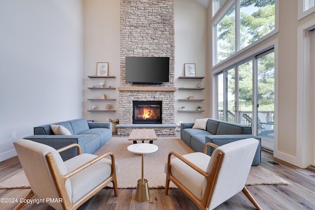 living area with baseboards, a towering ceiling, wood finished floors, and a stone fireplace