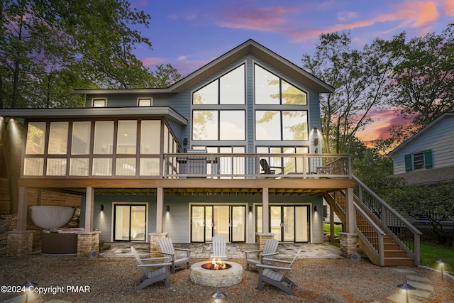 back of house at dusk featuring a deck, stairs, a sunroom, a patio area, and an outdoor fire pit