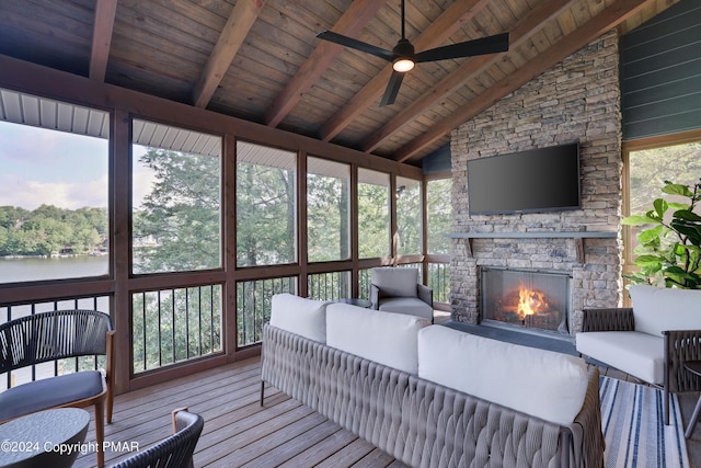 sunroom with ceiling fan, an outdoor living space with a fireplace, and beam ceiling
