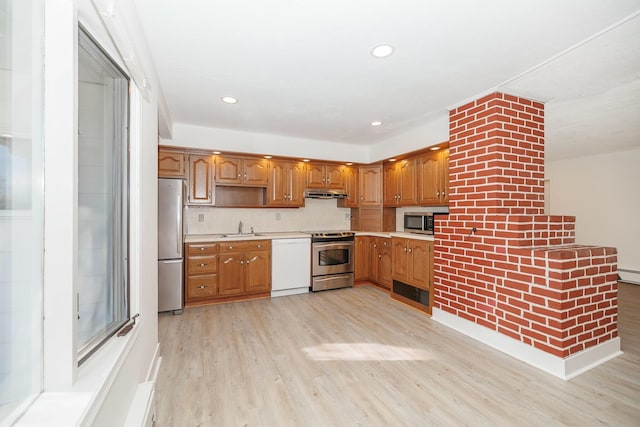 kitchen featuring a sink, under cabinet range hood, light wood-style floors, appliances with stainless steel finishes, and light countertops