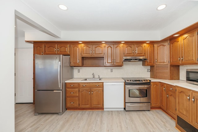 kitchen with a sink, stainless steel appliances, under cabinet range hood, and light wood finished floors