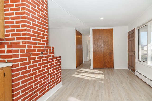 interior space with brick wall, a baseboard heating unit, baseboards, and wood finished floors