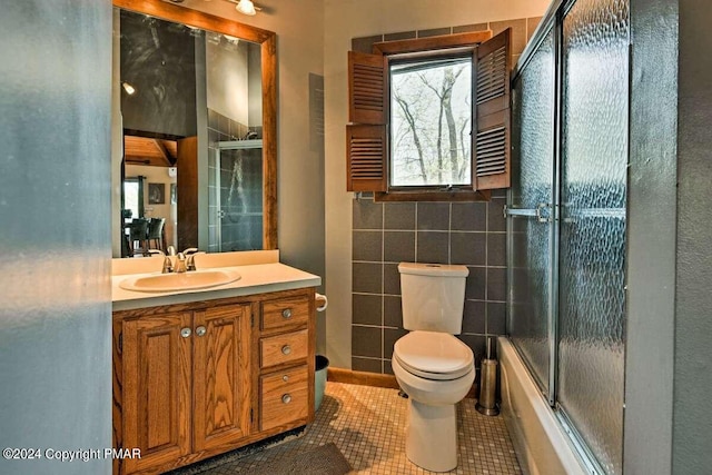 full bathroom featuring toilet, enclosed tub / shower combo, tile patterned floors, vanity, and tile walls