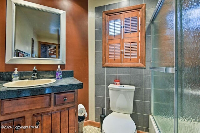 full bath featuring toilet, a shower with door, tile walls, and vanity