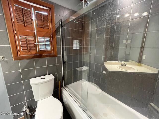 full bath with toilet, combined bath / shower with glass door, and tile walls