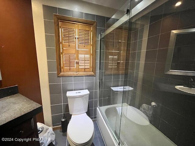 full bath with toilet, tile walls, and vanity