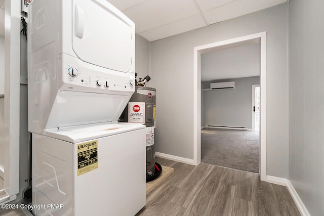 clothes washing area featuring water heater, a baseboard heating unit, stacked washing maching and dryer, wood finished floors, and baseboards