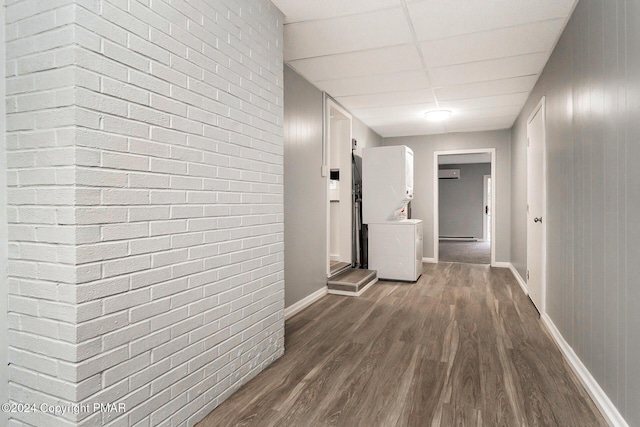 hall with a paneled ceiling, brick wall, dark wood-style flooring, baseboards, and an AC wall unit