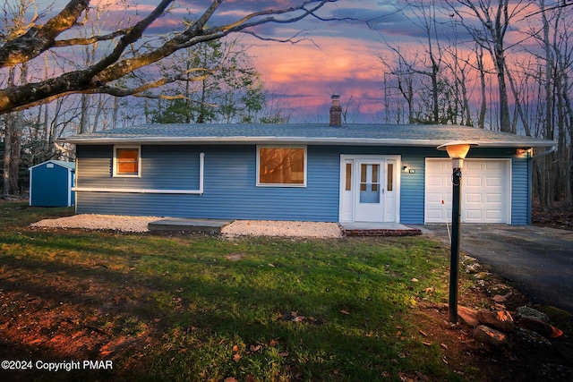 ranch-style home featuring an attached garage, a yard, driveway, a shed, and a chimney